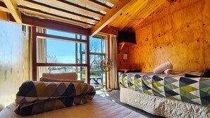 Um quarto de cabana aconchegante com uma cama, um banquinho com almofadas, um ventilador e vista para o exterior.