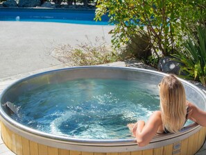 Una persona sentada en un jacuzzi de madera con una piscina al fondo.