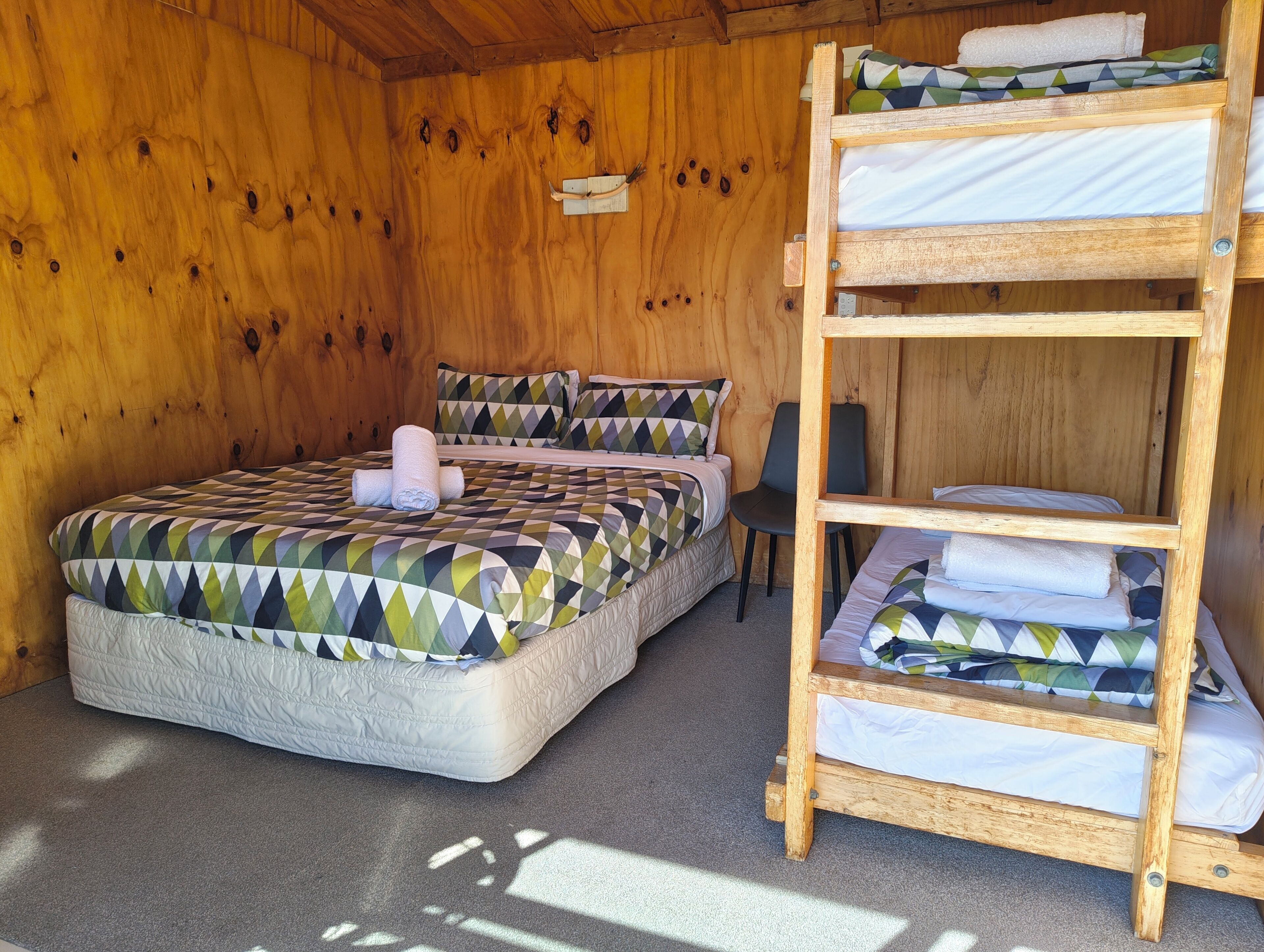 Una stanza in legno con un letto a castello, un letto singolo e una sedia.