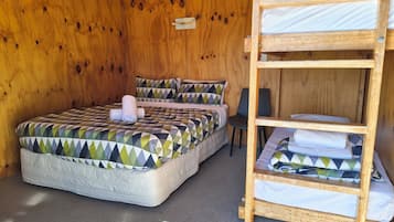 A wooden room with a bunk bed, a single bed, and a chair.
