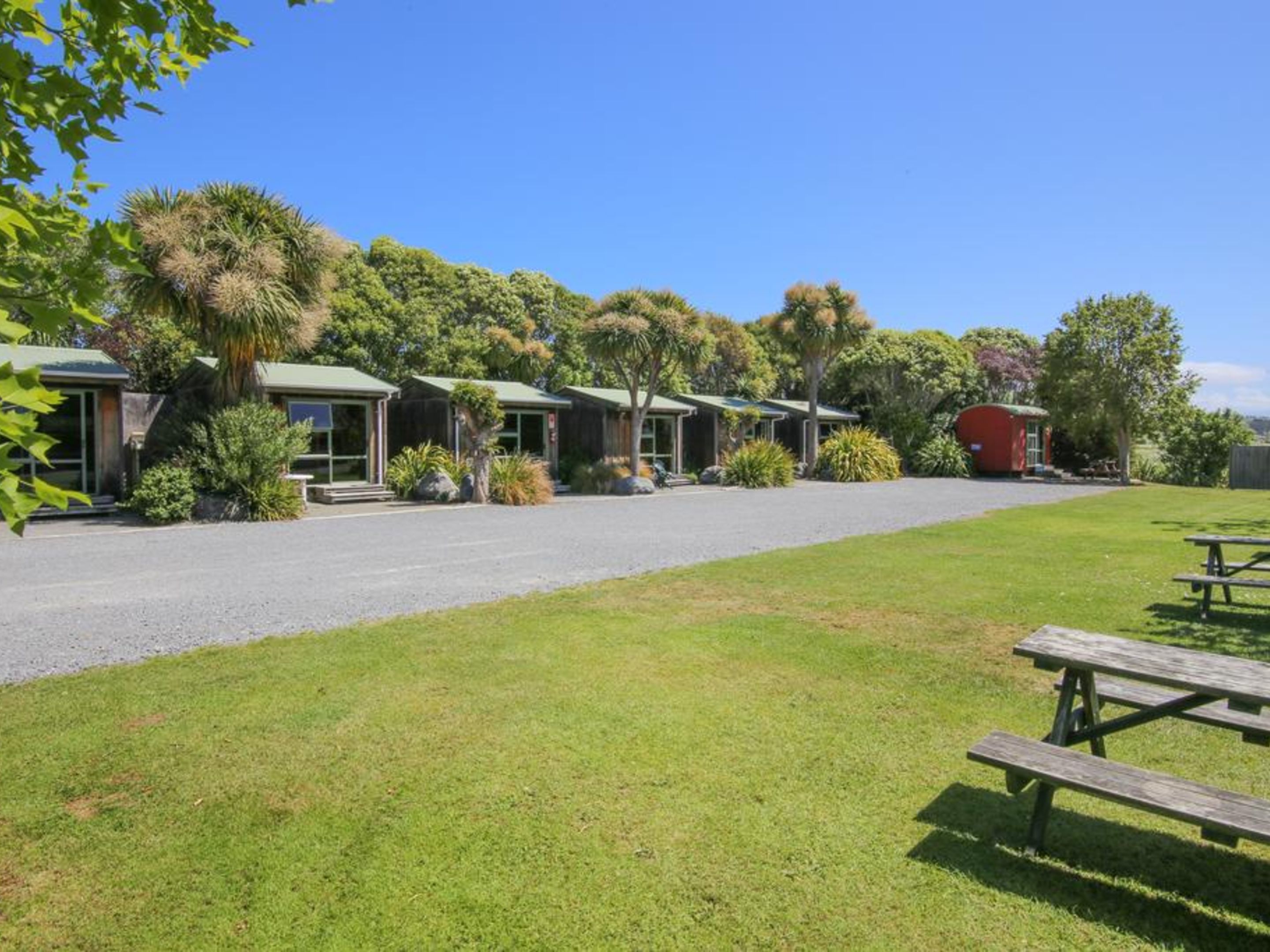 A row of single-story buildings with a gravel driveway, surrounded by lush greenery and trees.