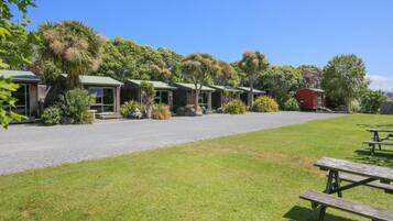 A row of single-story buildings with a gravel driveway, surrounded by lush greenery and trees.