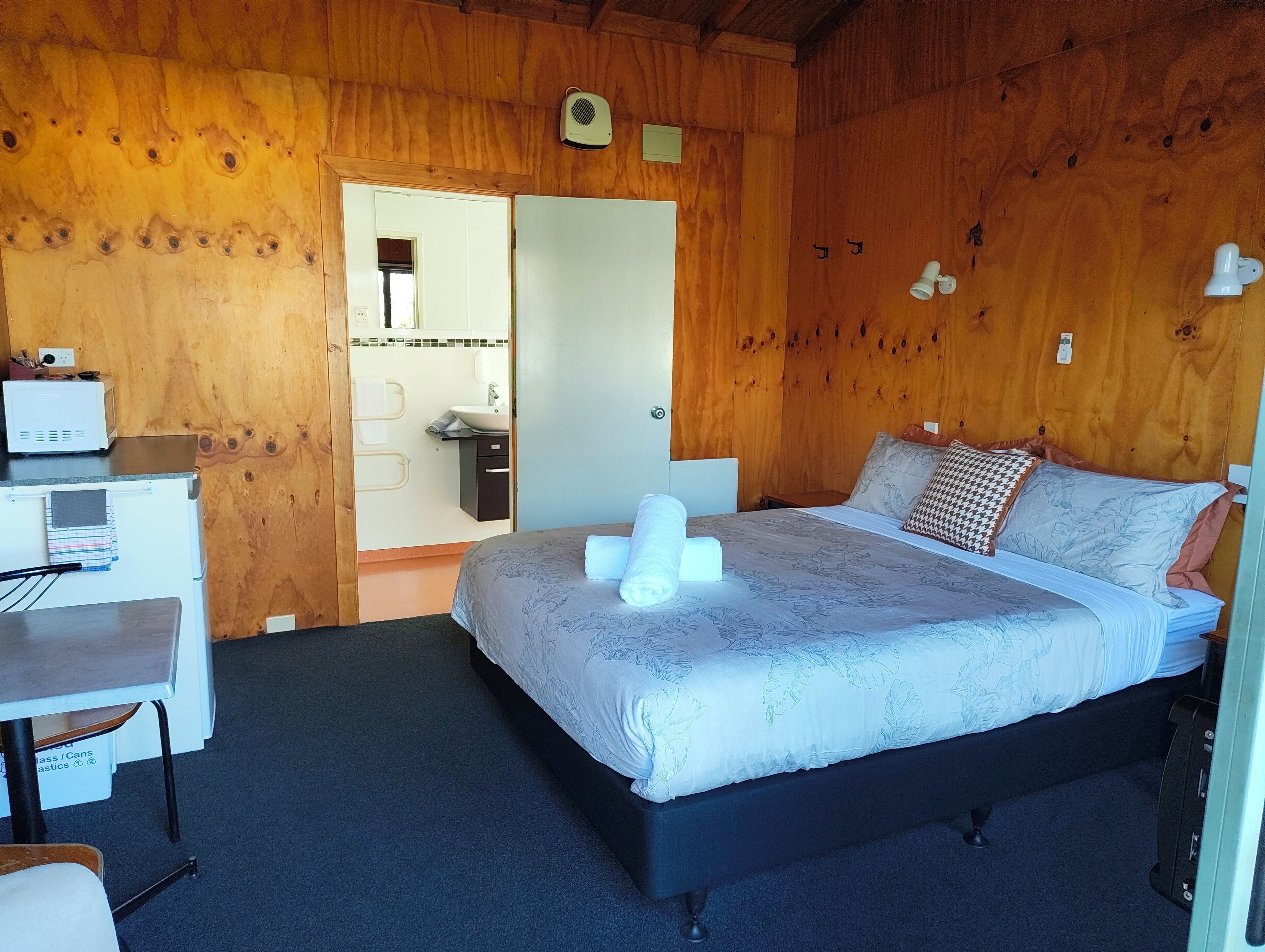 Een houten kamer met een bed, een bureau en een kleine badkamer.