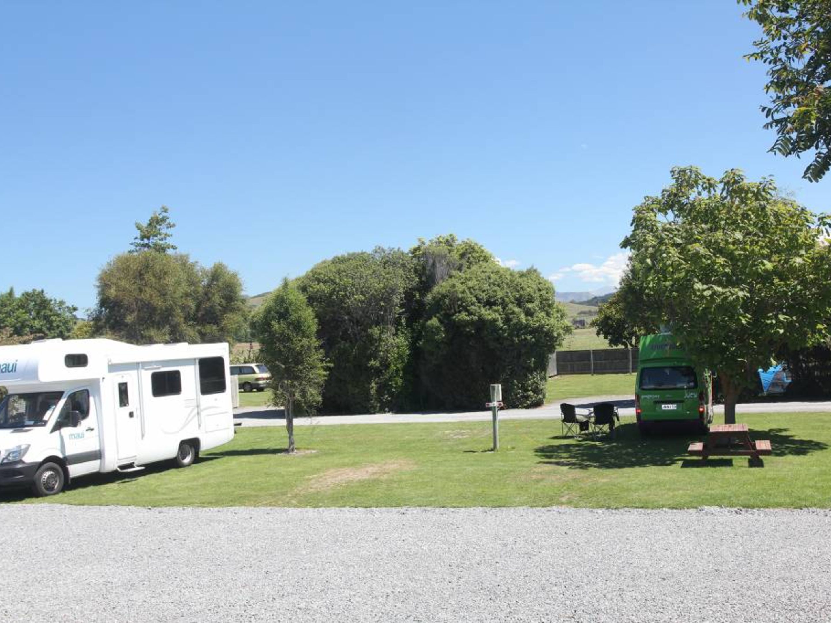 A campsite with RVs and a green bus parked on a grassy area with trees in the background.