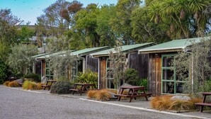 Uma fileira de cabanas de madeira rústica com telhados verdes, rodeadas por vegetação exuberante e mesas de piquenique.