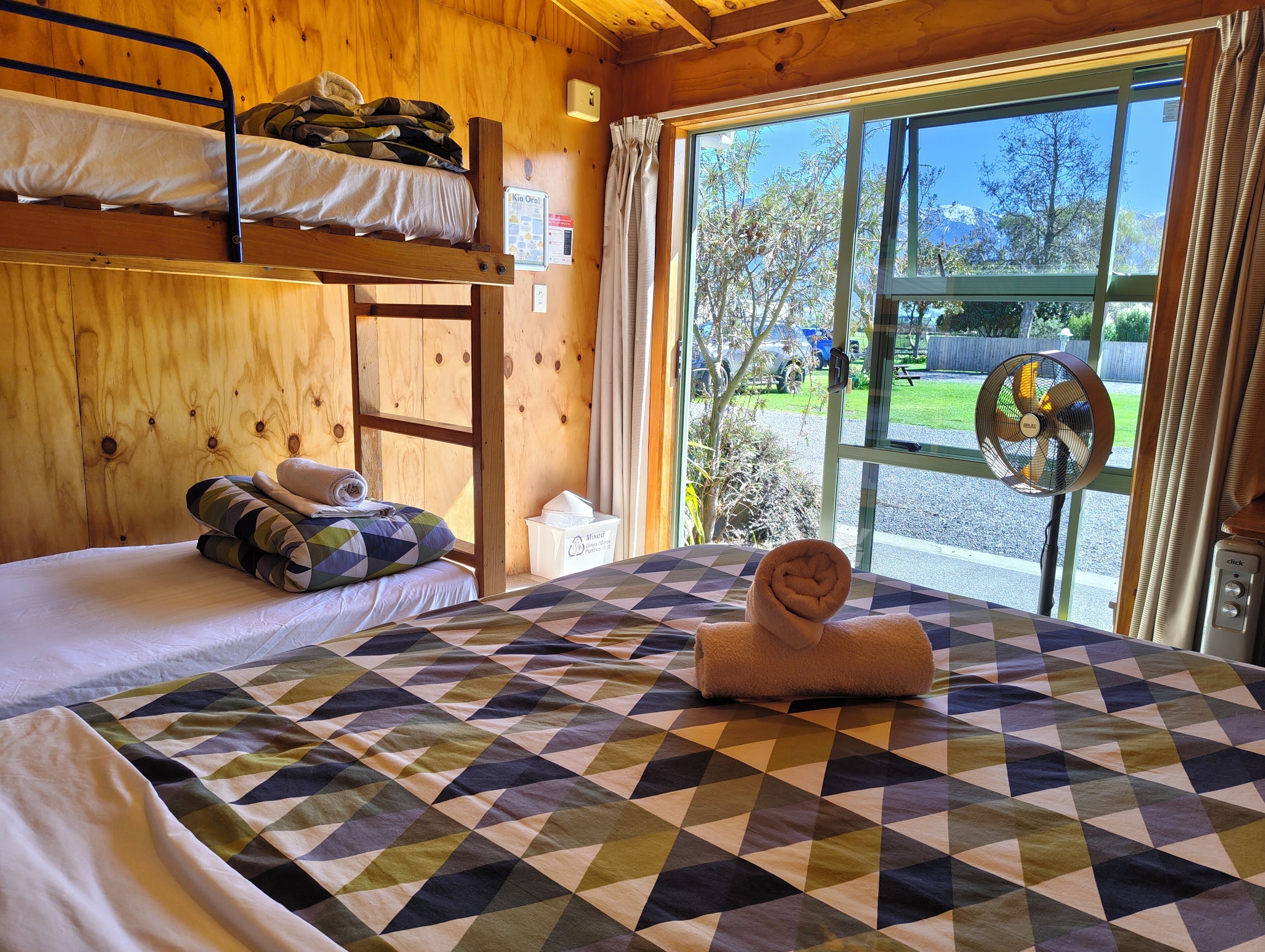 A wooden cabin room with bunk beds, a large window, and a view of the outdoors.