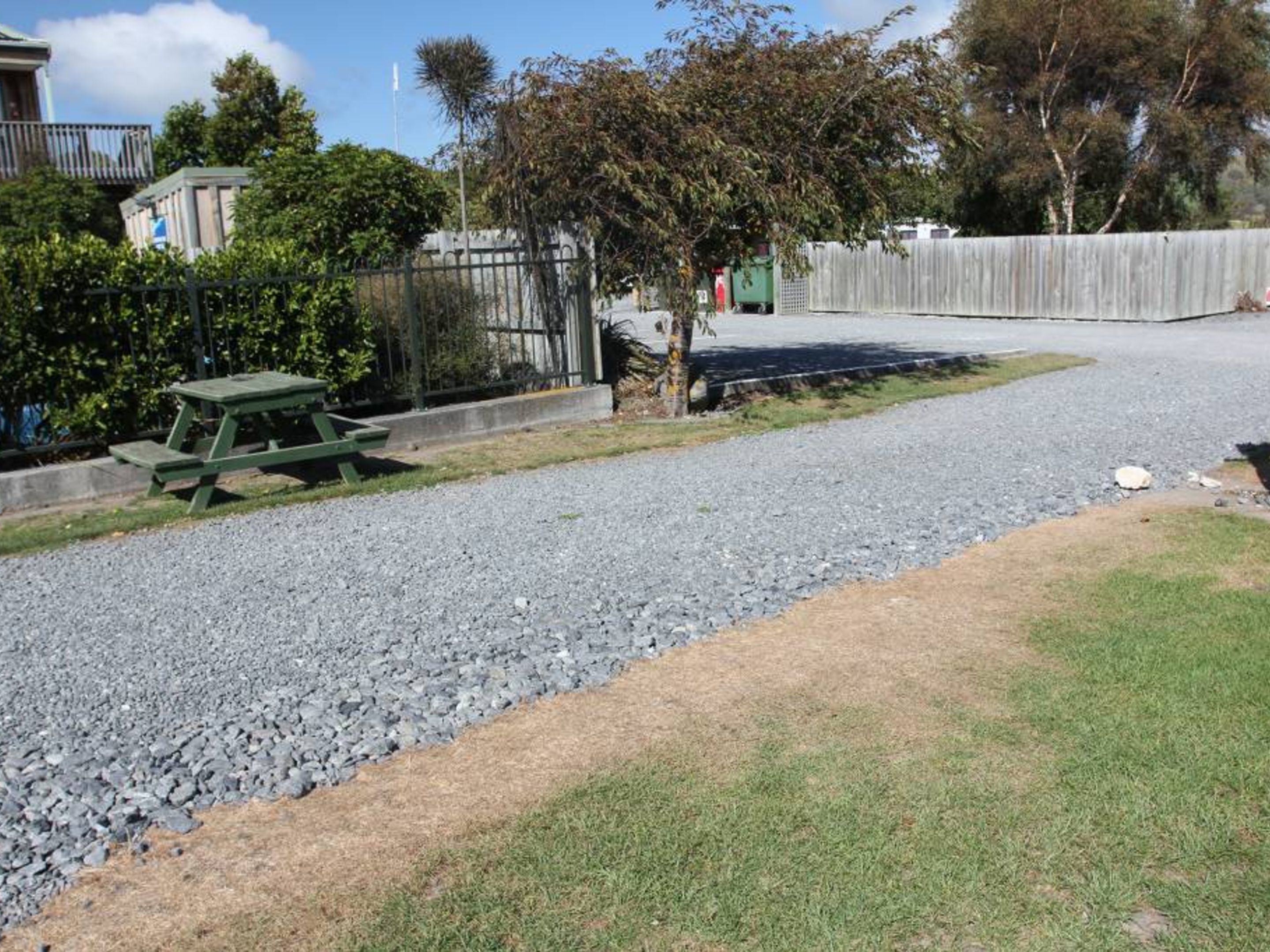 A gravel driveway leading to a house with a picnic table and a tree in the yard.