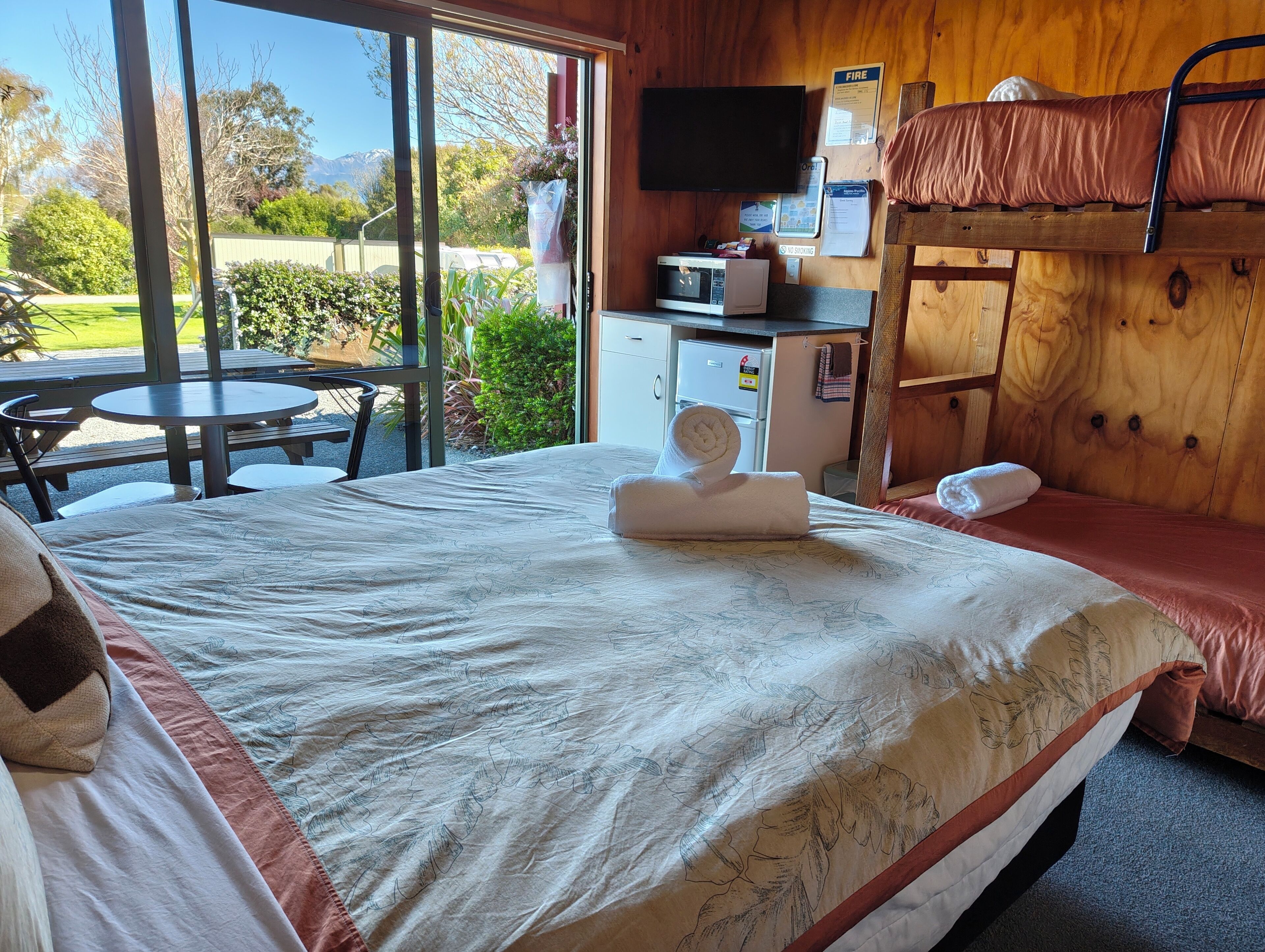 A hotel room with a bed, a bunk bed, a television, a microwave, and a small kitchenette.