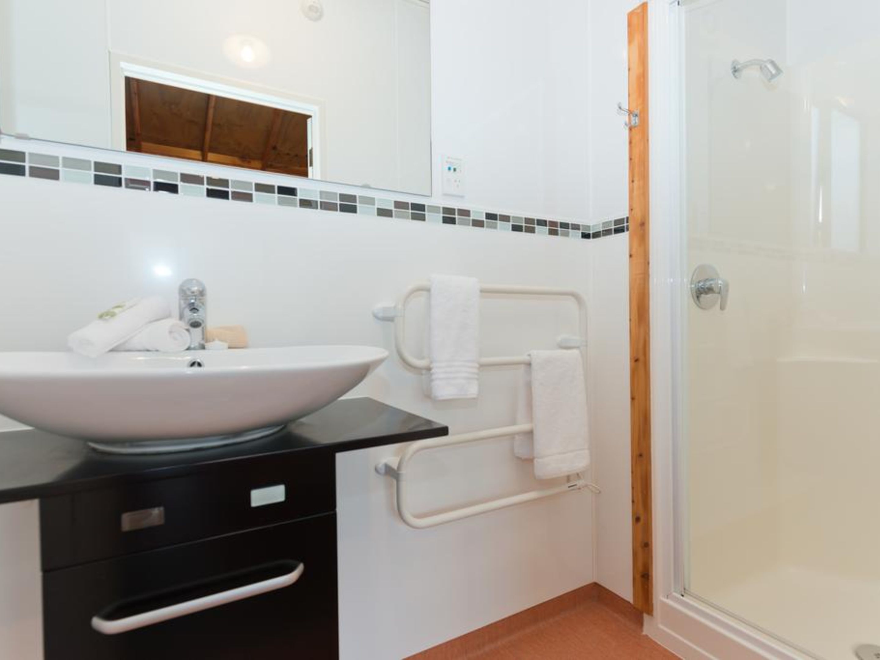 Een badkamer met een wit wastafelmeubel, een zwart aanrechtblad en een douchecabine met glazen wanden.