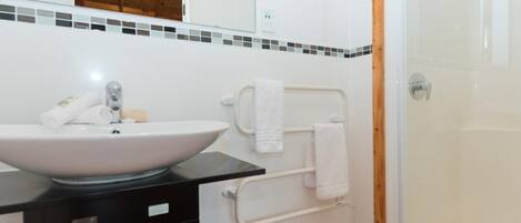 Un baño con lavamanos blanco, encimera negra y cabina de ducha de vidrio.