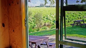 Uma porta de madeira dá para uma mesa de piquenique e outra mesa de piquenique em uma área gramada com um rio.