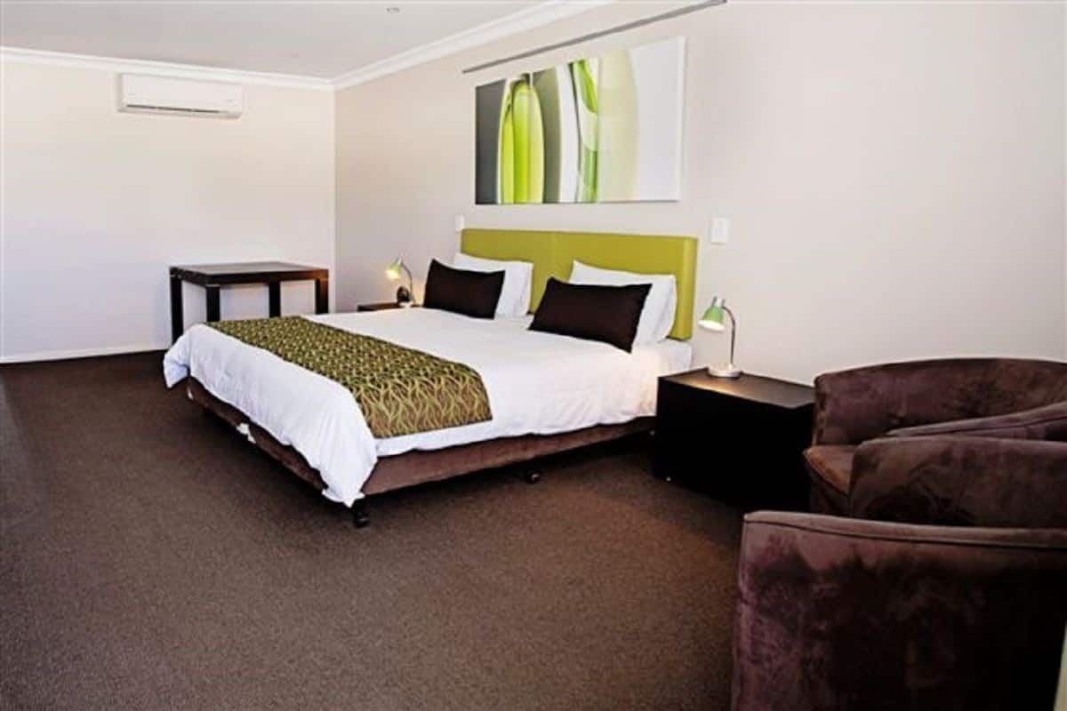 A hotel room with a bed, bedside tables, a lamp, and a chair.
