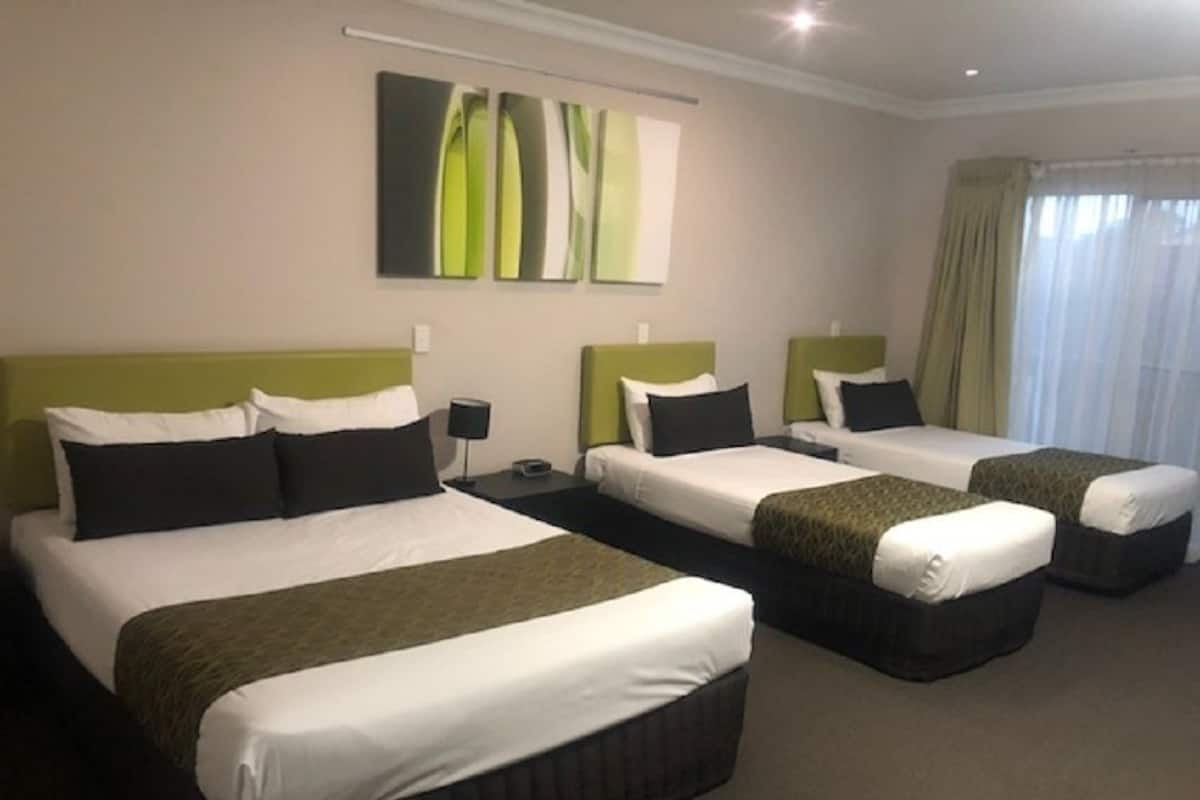 A hotel room with three beds, each with white bedding and green headboards. There is a large abstract painting on the wall above the beds.