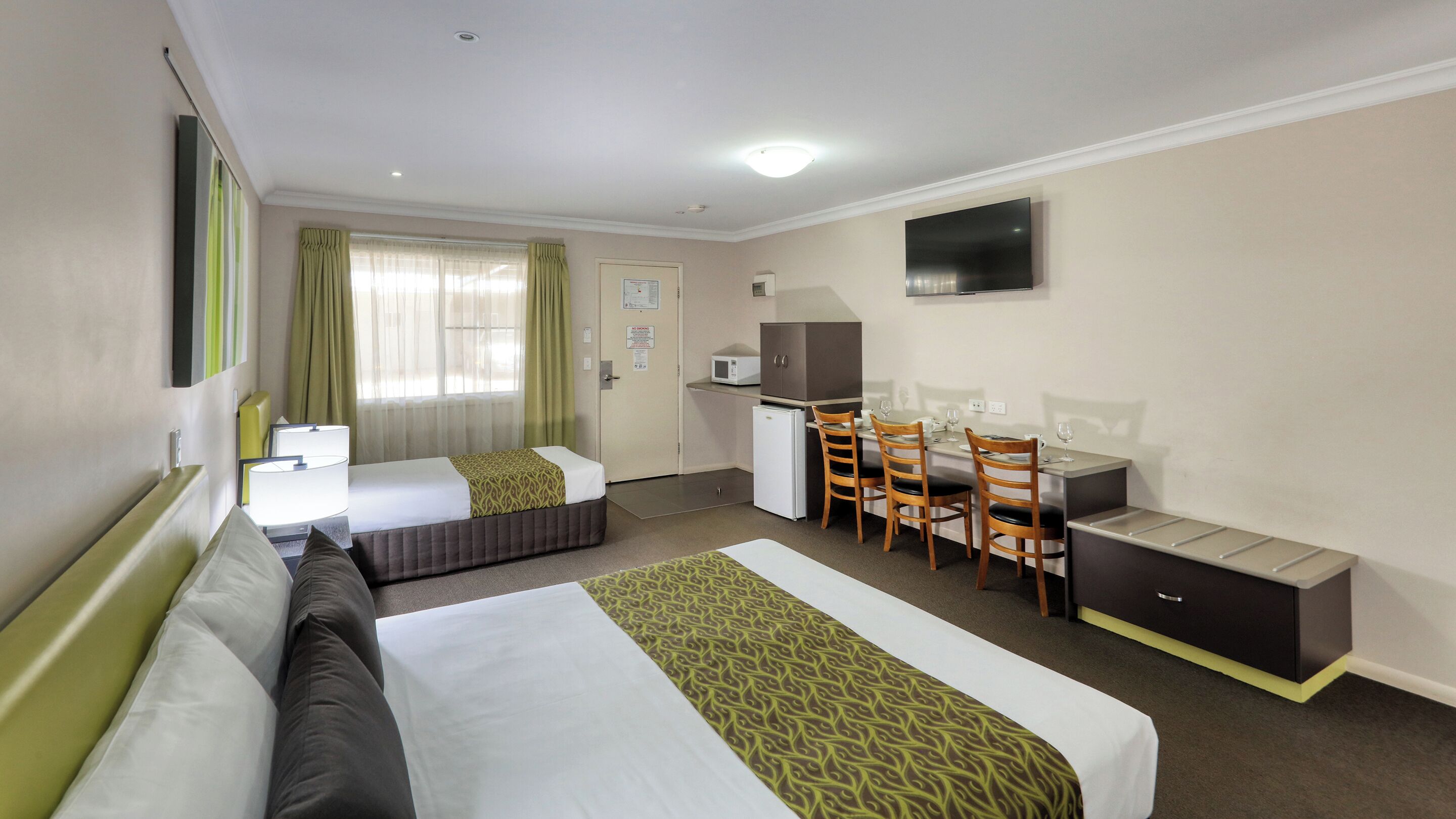 A hotel room with two beds, a desk, a chair, a television, and a microwave.