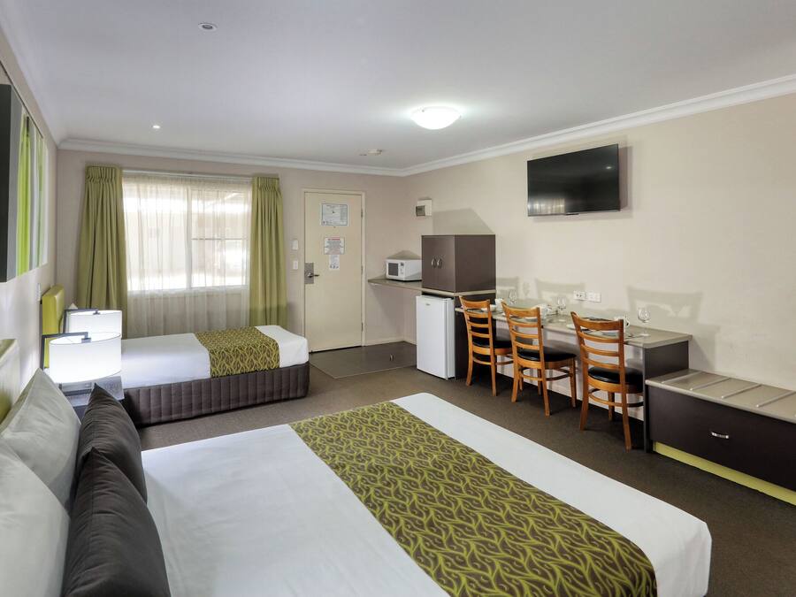 A hotel room with two beds, a desk, a chair, a television, and a microwave.