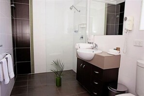 A modern bathroom with a large mirror, a white sink, a hairdryer, and a potted plant.