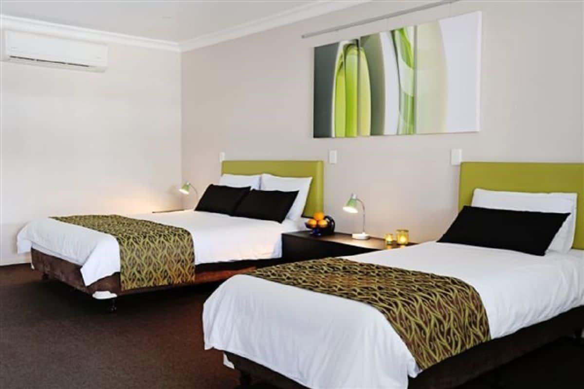 A hotel room with two single beds, each with a patterned bedspread and pillows, a bedside table with a lamp, and a wall-mounted artwork.