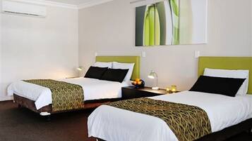 A hotel room with two single beds, each with a patterned bedspread and pillows, a bedside table with a lamp, and a wall-mounted artwork.