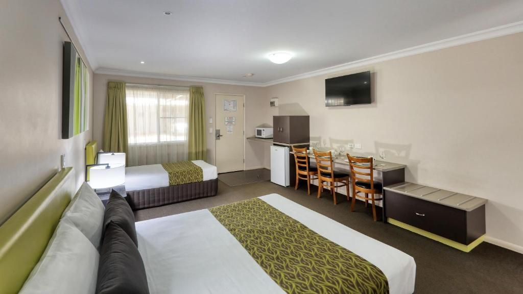 Habitación de hotel con dos camas, un escritorio con sillas, televisión y una pequeña kitchenette.