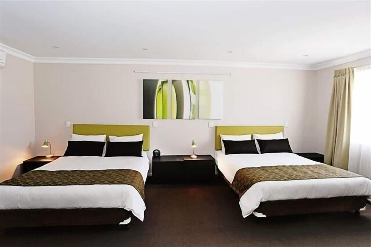 A hotel room with two beds, a headboard, a nightstand, a lamp, and a painting on the wall.