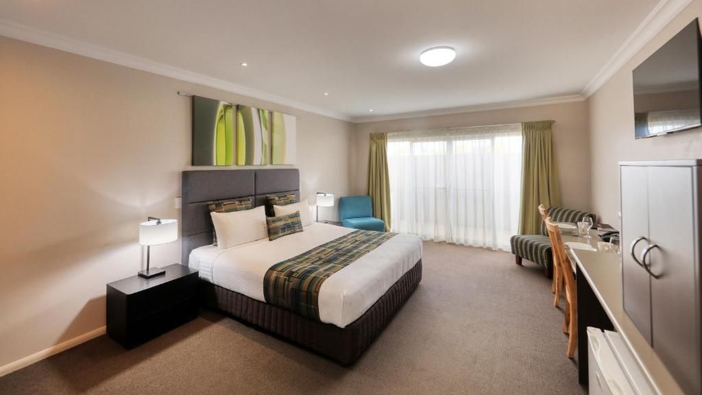 Een hotelkamer met een bed, nachtkastje, lamp, stoel en een televisie.