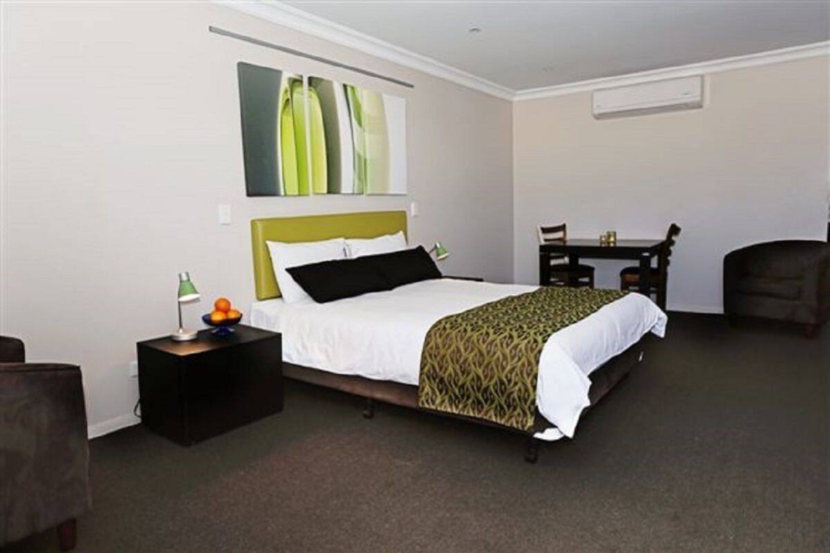 A hotel room with a bed, bedside table, lamp, and a small table with chairs.