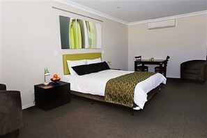 A hotel room with a bed, bedside table, lamp, and a small table with chairs. - Drover's Motor Inn, Dalby (Dalby)