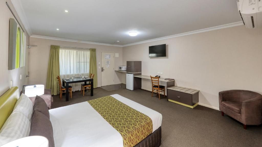 A hotel room with a bed, desk, chair, and a television on the wall.