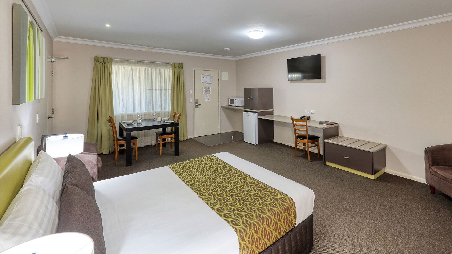 Une chambre d’hôtel équipée d’un lit, d’un bureau, d’une chaise, d’une télévision et d’une petite kitchenette.
