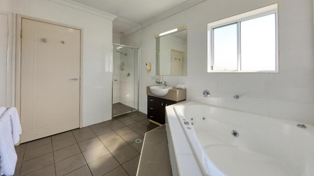 A modern bathroom with a large bathtub, a shower, a sink, and a mirror.