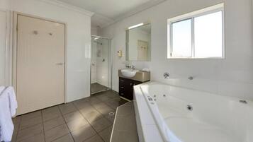 Un baño moderno con una bañera grande, ducha, lavamanos y espejo.