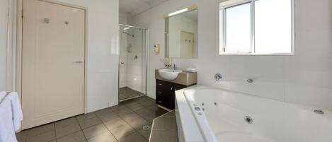 A modern bathroom with a large bathtub, a shower, a sink, and a mirror.