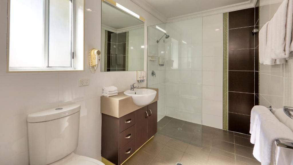 Un baño moderno con inodoro, lavabo, espejo y ducha.