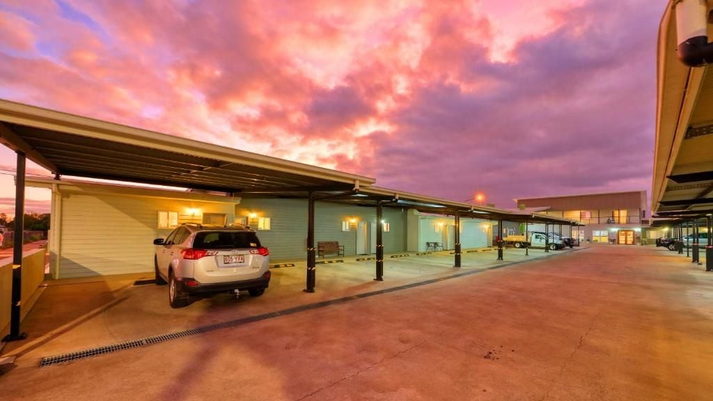 Un área de estacionamiento con un automóvil, estructuras cubiertas y un edificio con luces encendidas.