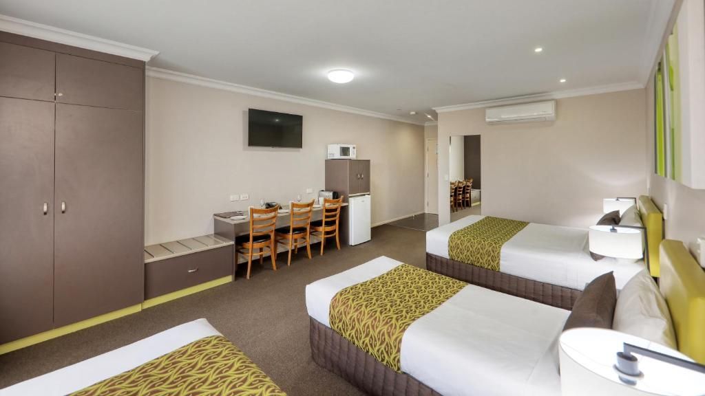 A hotel room with two beds, a desk with chairs, a television, and a wardrobe.