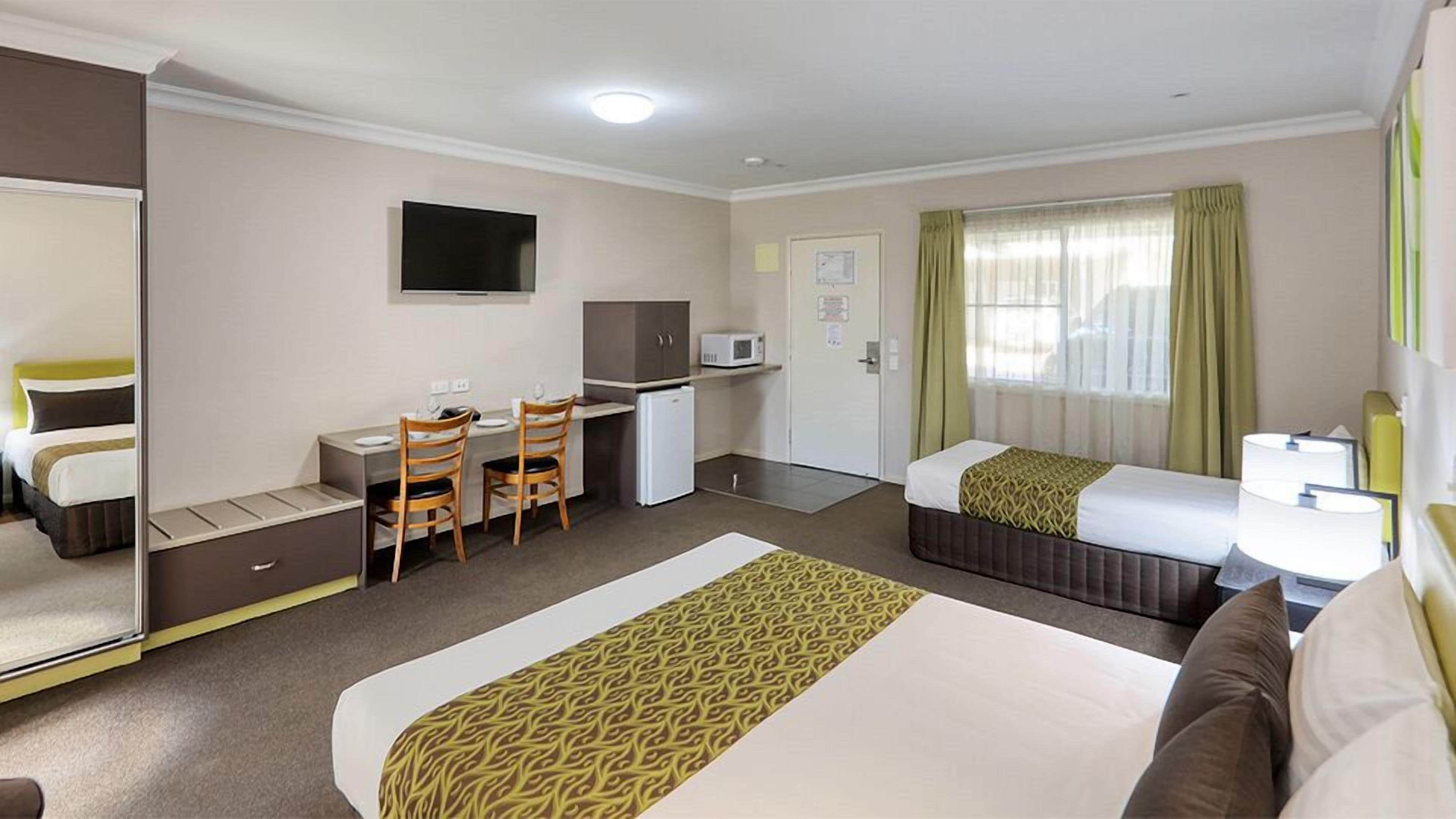 A hotel room with a bed, desk, chairs, a television, a microwave, and a door.