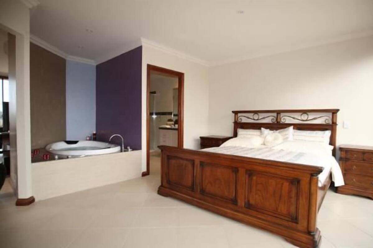 A bedroom with a wooden bed, a large window, and a bathroom with a bathtub.