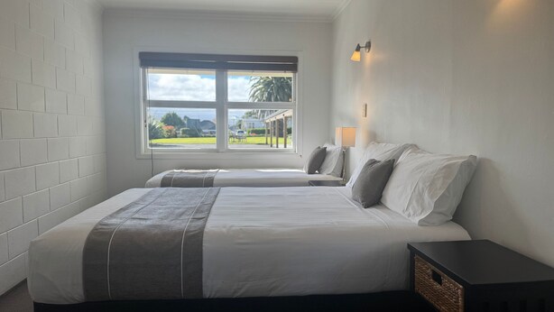 Ein Schlafzimmer mit zwei Betten, einem großen Fenster mit Blick ins Freie, einem Nachttisch mit Lampe und einem kleinen Beistelltisch.