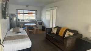 Ein gemütlicher Raum mit Bett, Schlafsofa, kleinem Tisch und Küchenzeile.