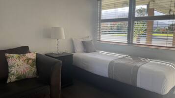 Une chambre à coucher avec un lit, une table de chevet, une lampe et une fenêtre avec des stores.