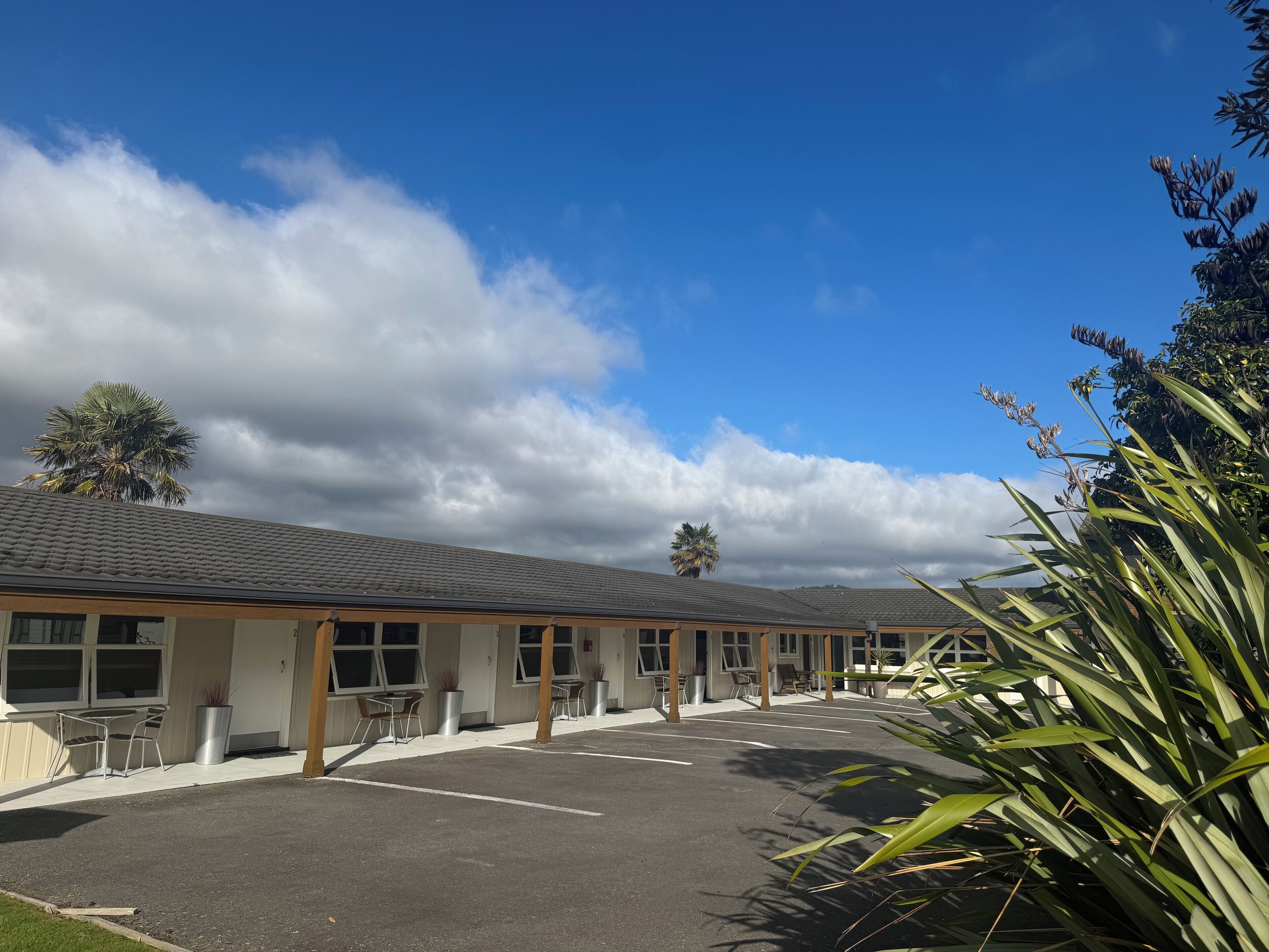 A hotel with a covered outdoor seating area, a parking lot, and a clear sky.