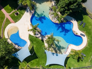An aerial view of a swimming pool complex with multiple interconnected pools, surrounded by well-maintained grass and palm trees. - Tasman Holiday Parks - Merool on the Murray (Moama)