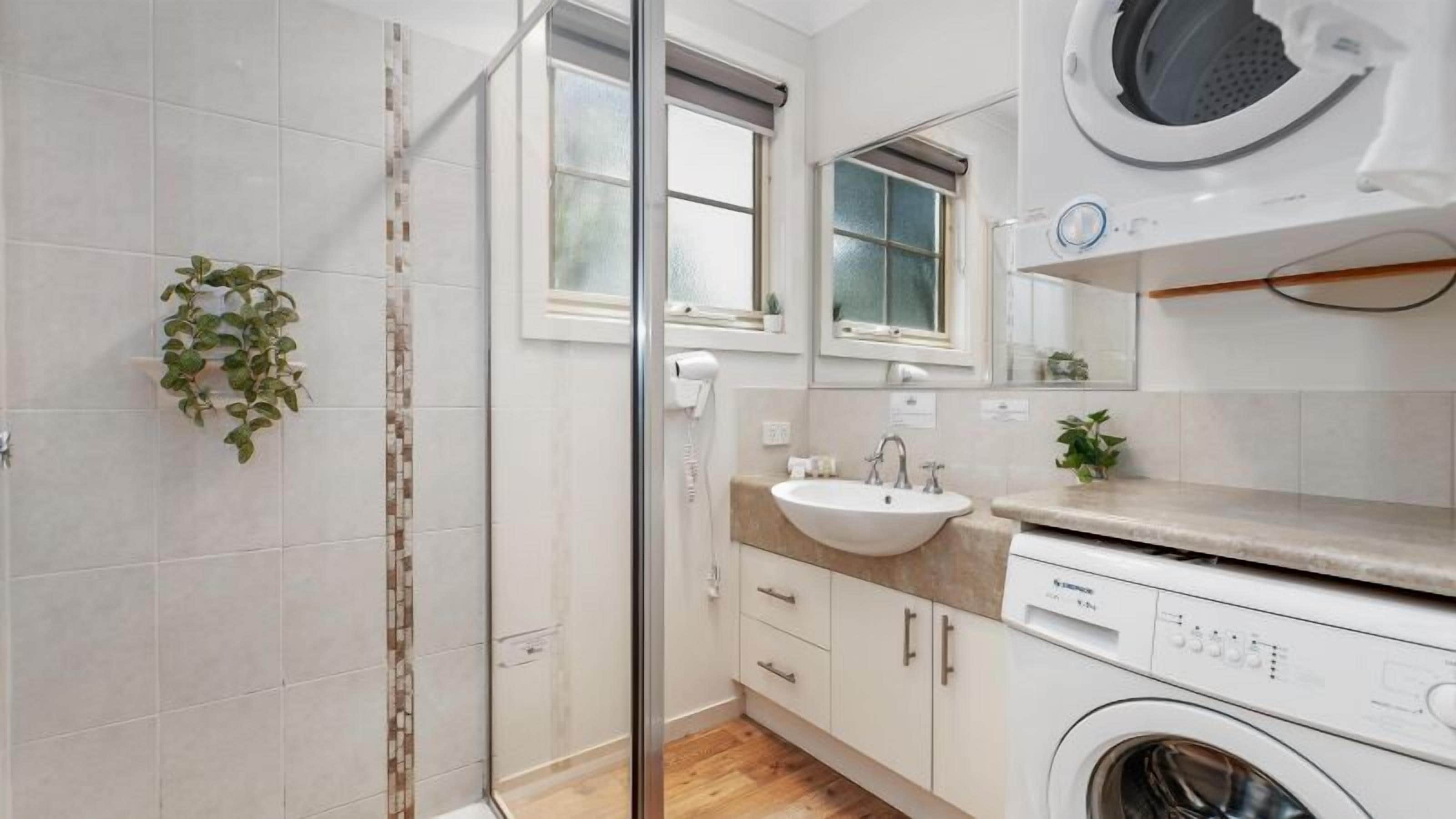 Un baño moderno con cabina de ducha de vidrio, un lavamanos con espejo y una lavadora.