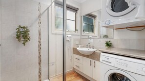 A modern bathroom with a glass shower enclosure, a sink with a mirror above, and a washing machine.
