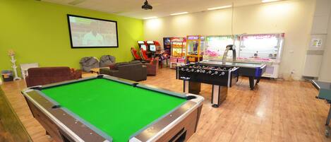 A pool table, a foosball table, and arcade games in a room with green walls and wooden flooring.