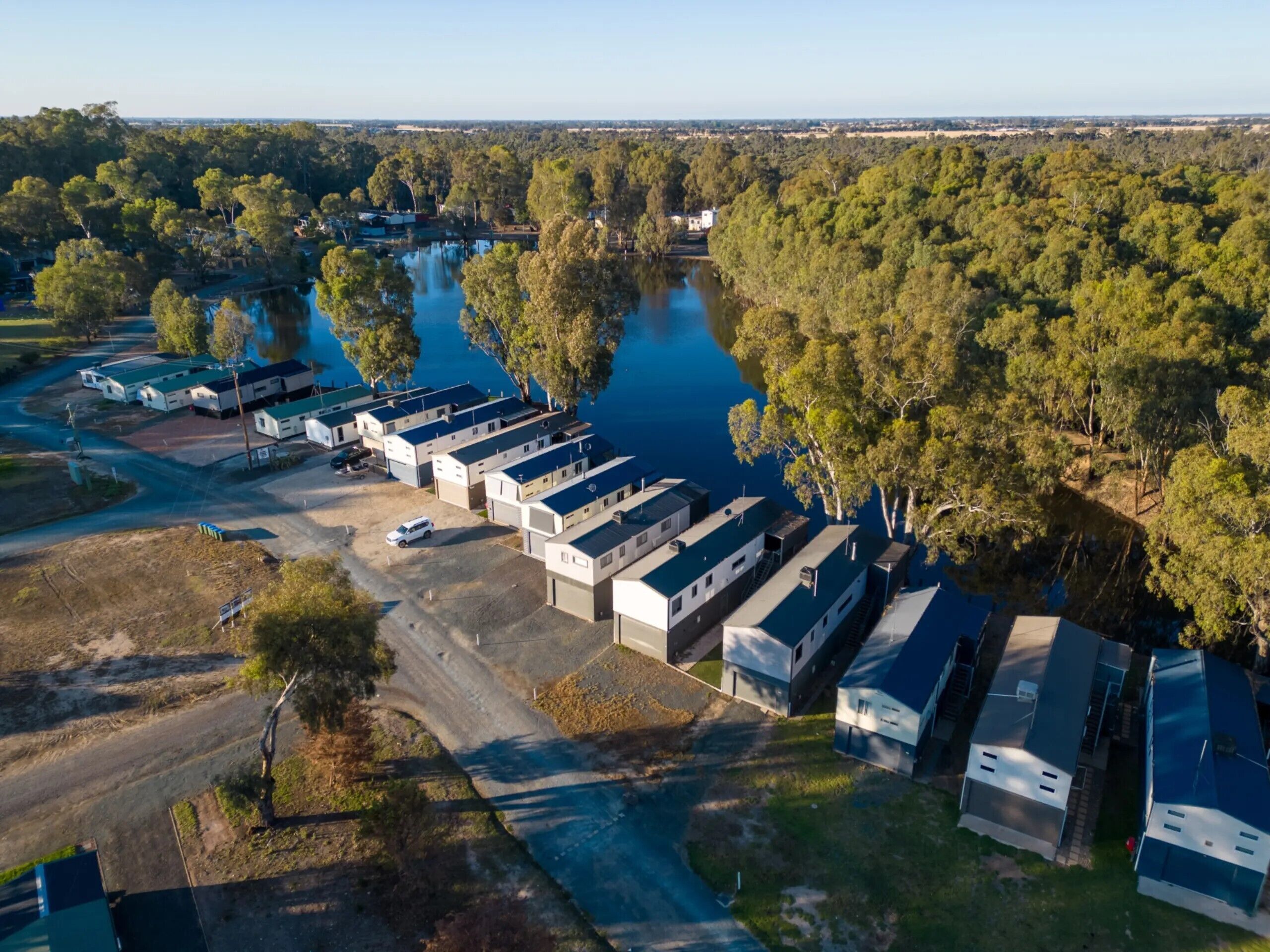 An aerial view of a caravan park with multiple caravans, a lake, and surrounding trees.