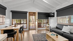 Ein modernes Wohnzimmer mit Essbereich, großen Fenstern und einem schwarzen Sofa.