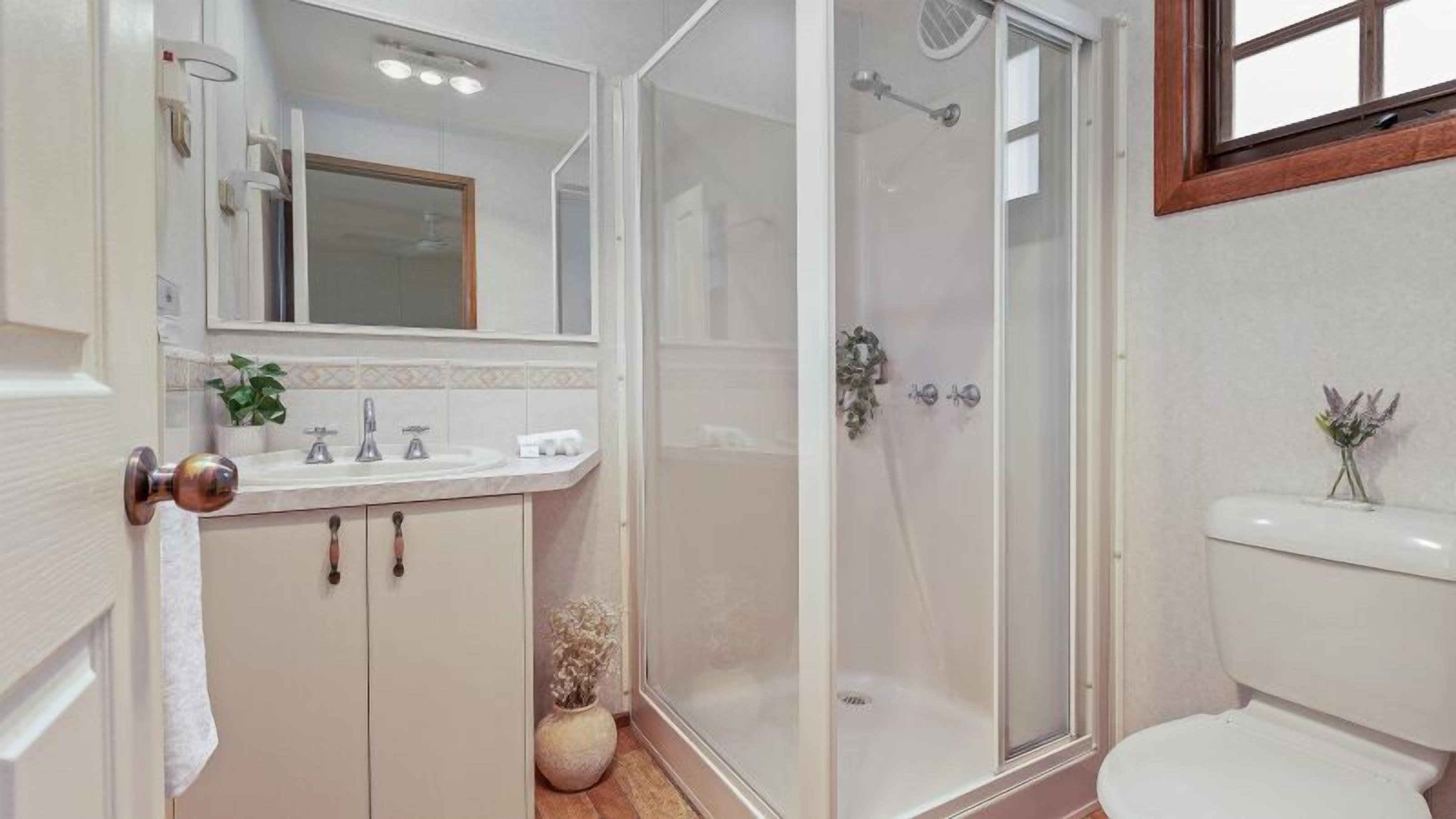 A bathroom with a shower, toilet, sink, and mirror.