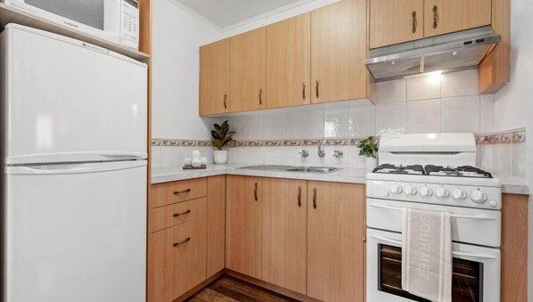A compact kitchen with wooden cabinets, a white refrigerator, a stove, and a sink.