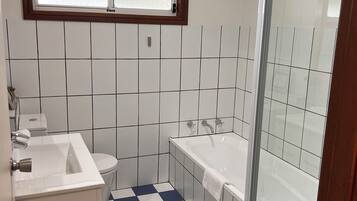 Et badeværelse med et skakternet gulv, et vindue over vasken og en brusekabine med glasvægge.